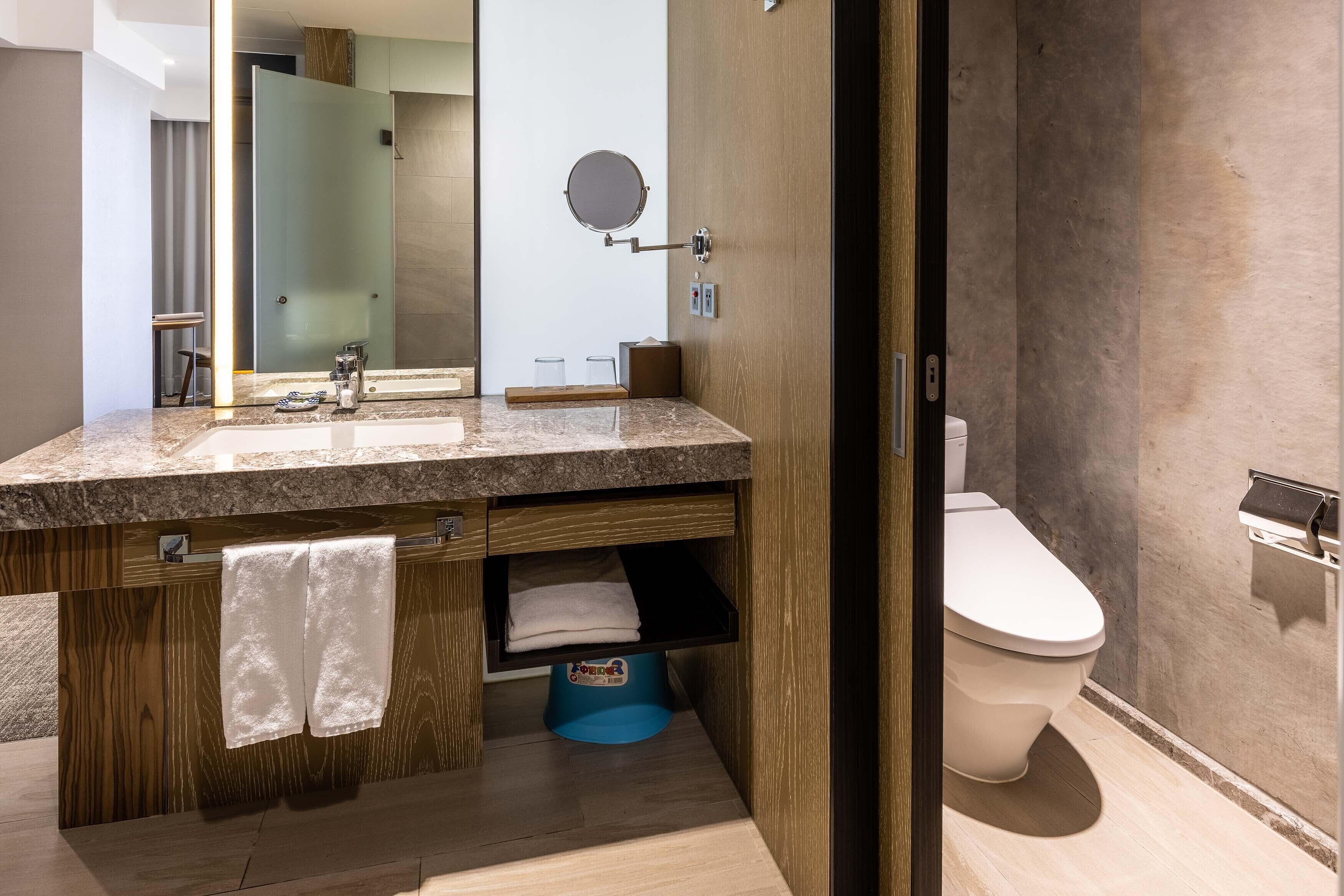 A modern bathroom with a granite countertop, wooden vanity, a mirror, and a toilet.