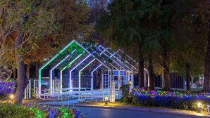 A glasshouse structure with a metal frame and white railings, surrounded by trees and illuminated by colorful lights. - Hsin Hotel (Chiayi City)