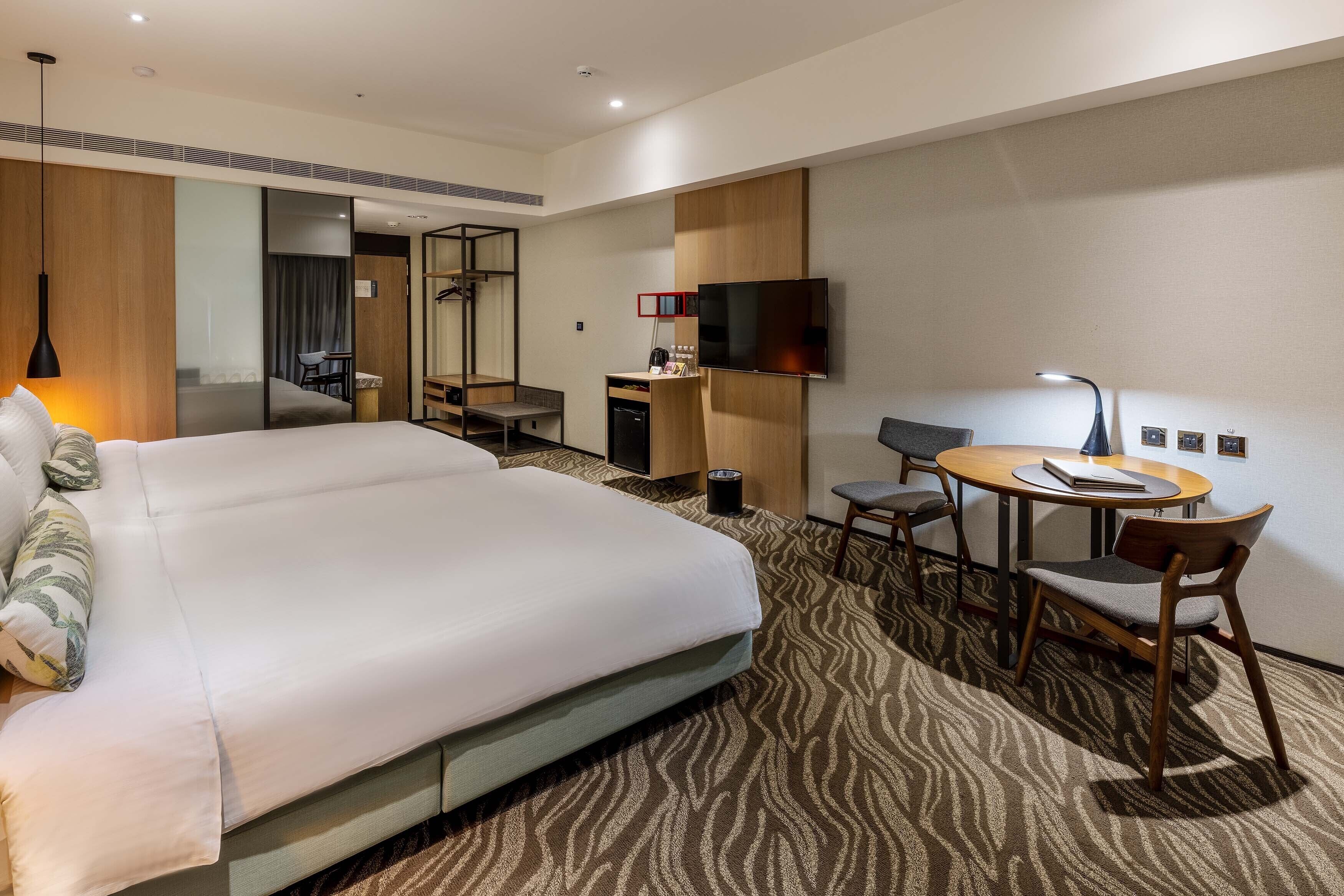 Una habitación de hotel con una cama grande, un escritorio, una silla, un televisor y un espejo.