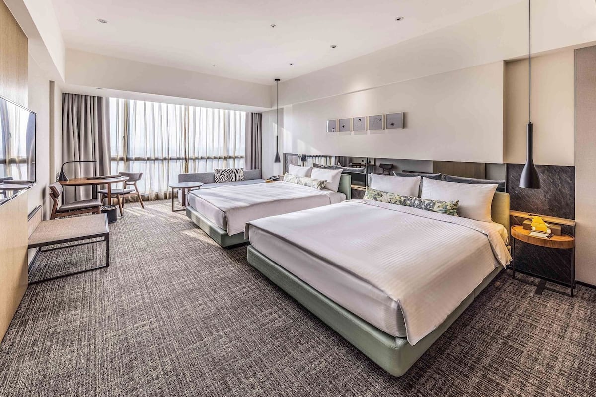 A hotel room with two beds, a desk, a chair, and a large window with curtains.