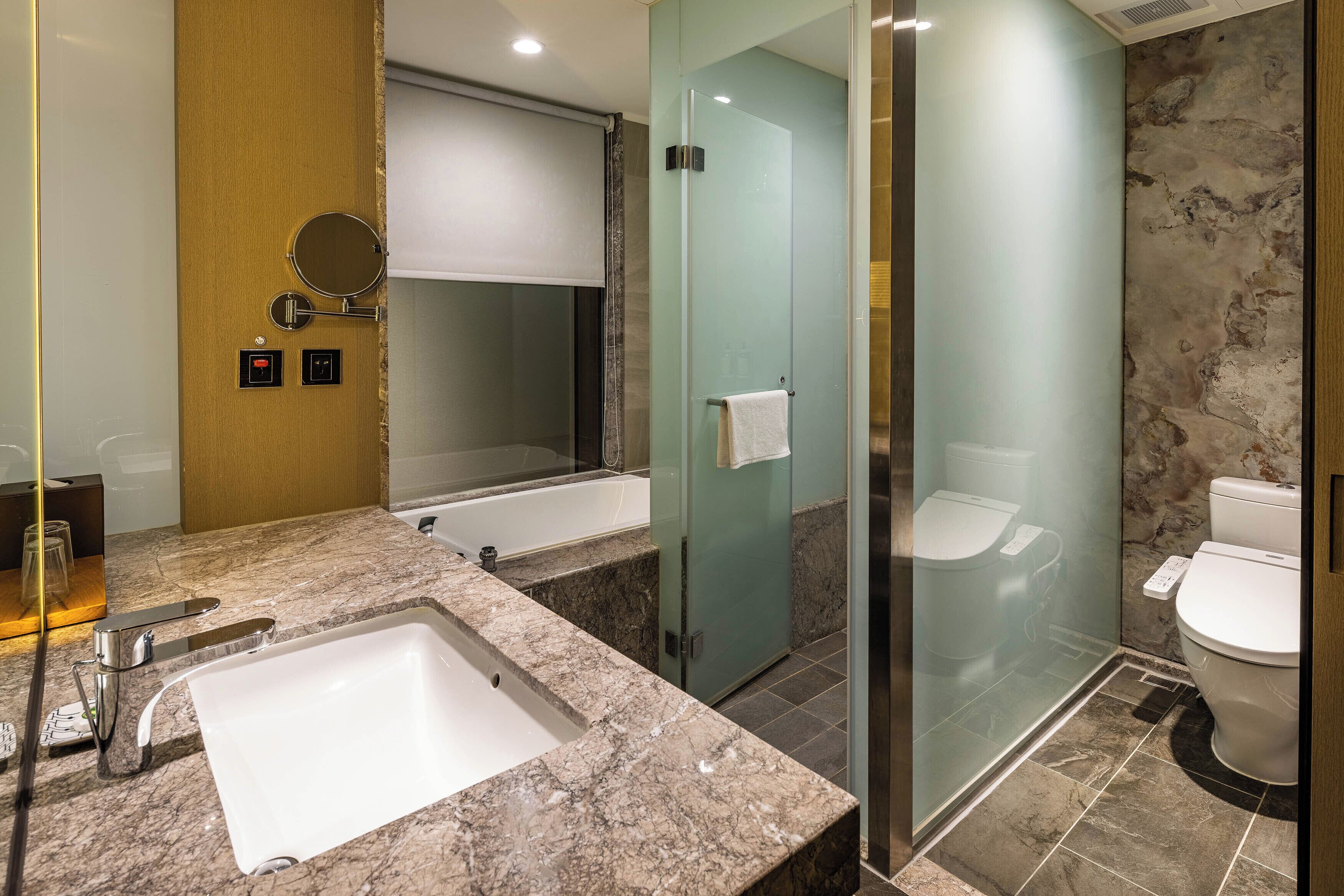 A modern bathroom with a marble sink, a bathtub, a glass-enclosed shower, and a toilet.