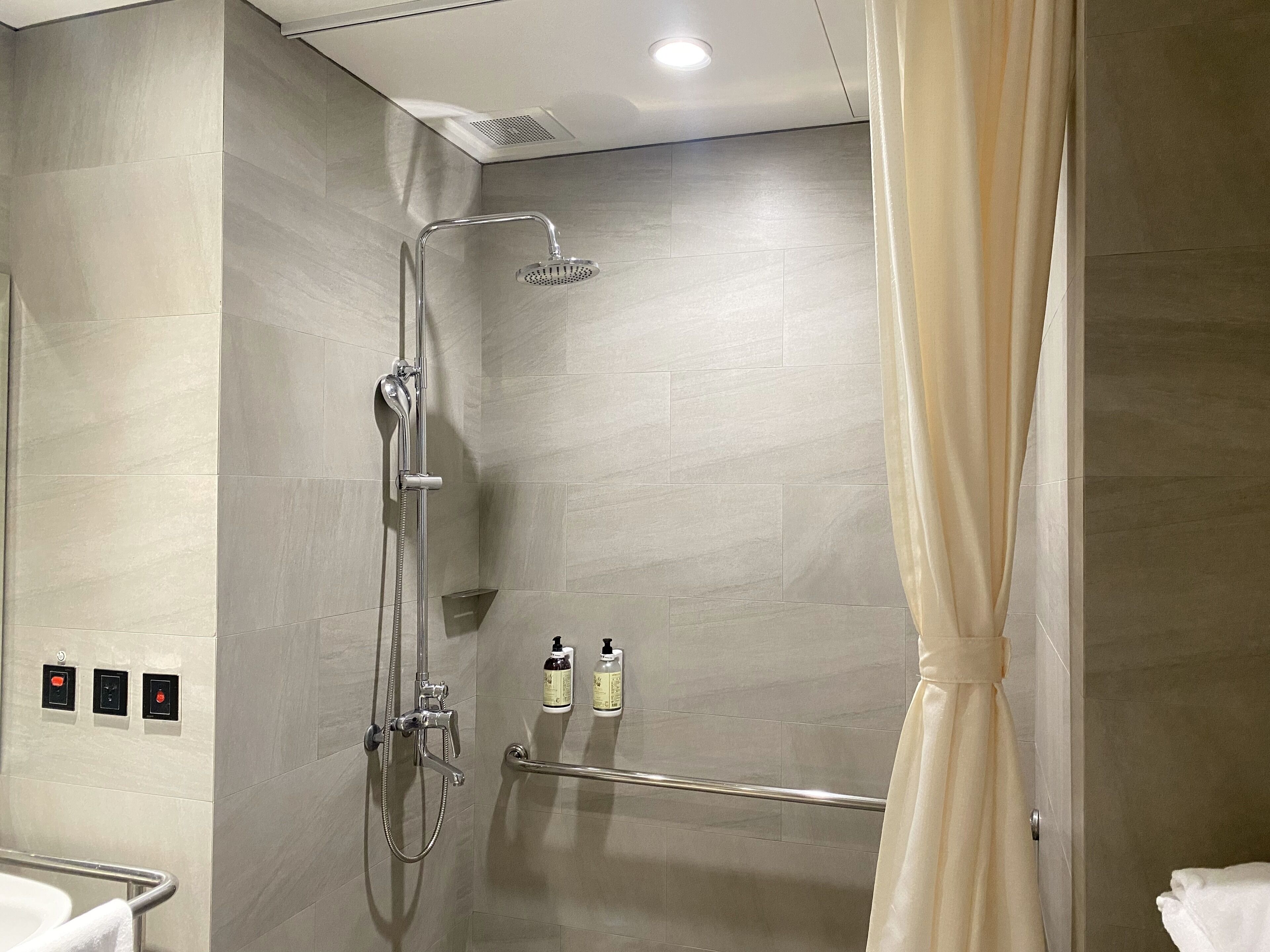 Un baño moderno con ducha, repisa de vidrio con artículos de aseo y un perchero para toallas.