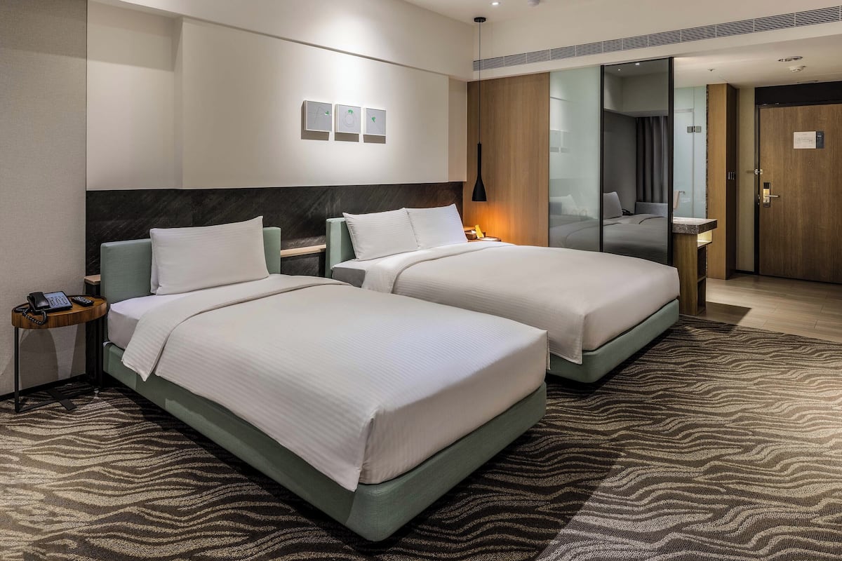 A hotel room with two beds, a bedside table with a phone, a mirror, and a door.