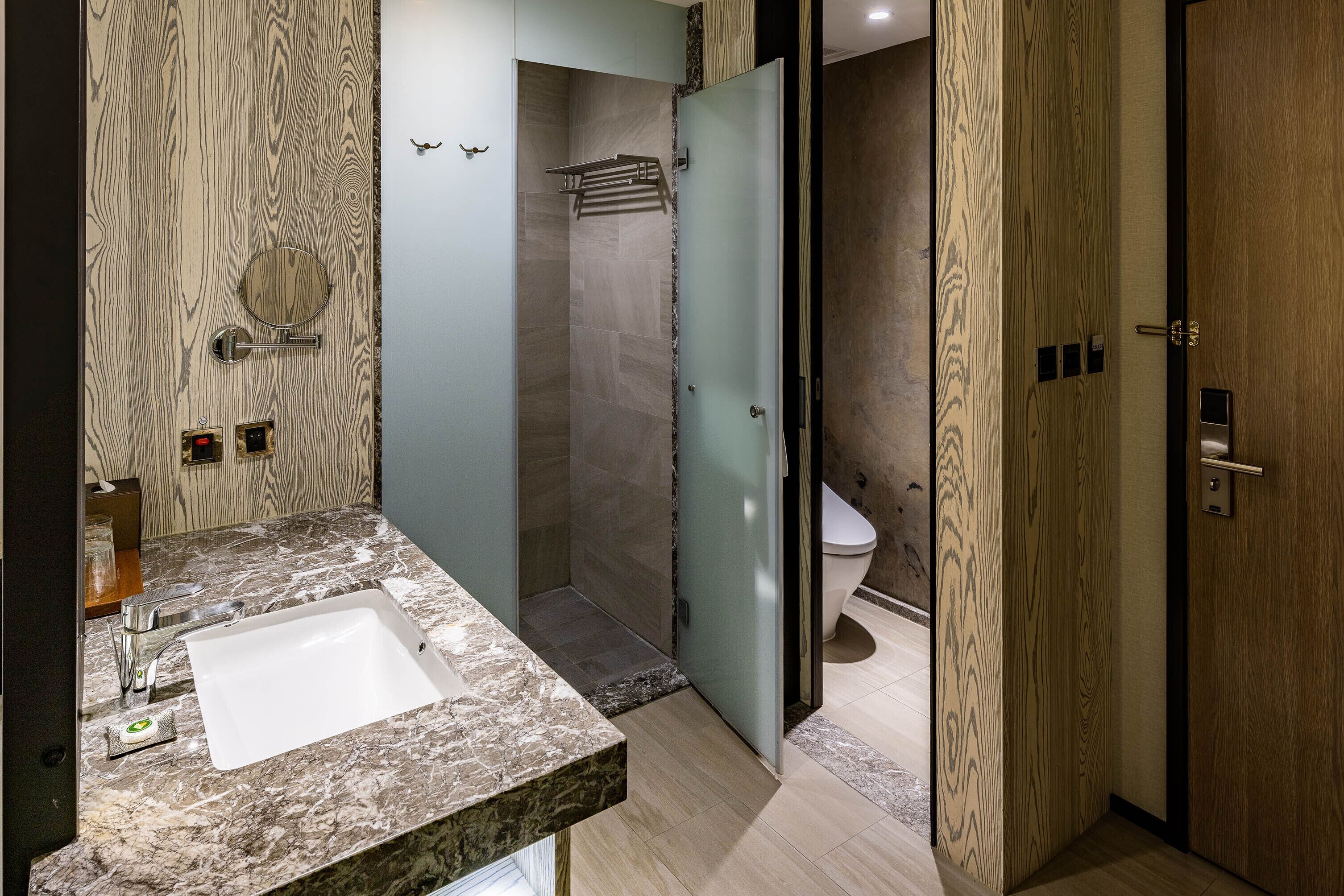 Un baño moderno con lavamanos de mármol, cabina de ducha con mampara de cristal y puerta de madera.