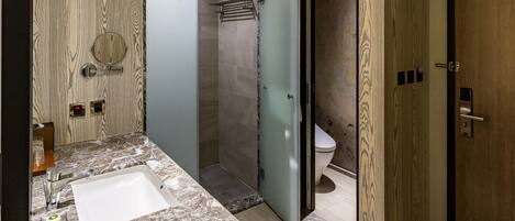 Un baño moderno con lavamanos de mármol, cabina de ducha con mampara de cristal y puerta de madera.