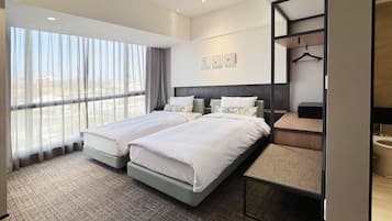 A hotel room with two beds, a large window with sheer curtains, a mirror, and a small table.