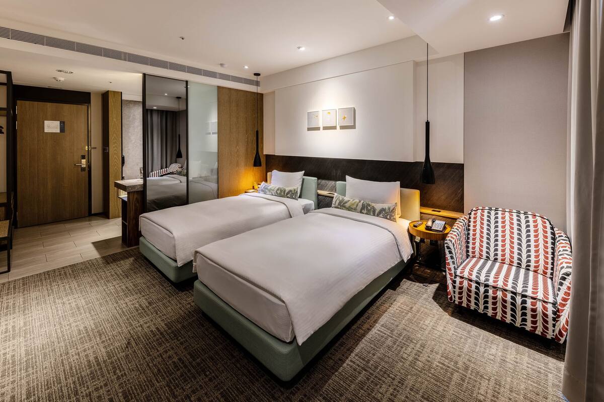 A hotel room with two beds, a sofa, a desk, and a mirror.
