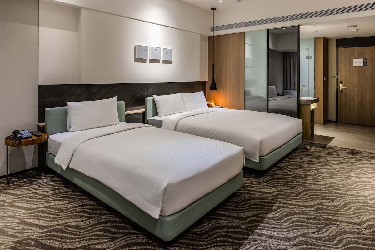 A hotel room with two beds, a bedside table with a phone, a mirror, and a wall-mounted artwork.