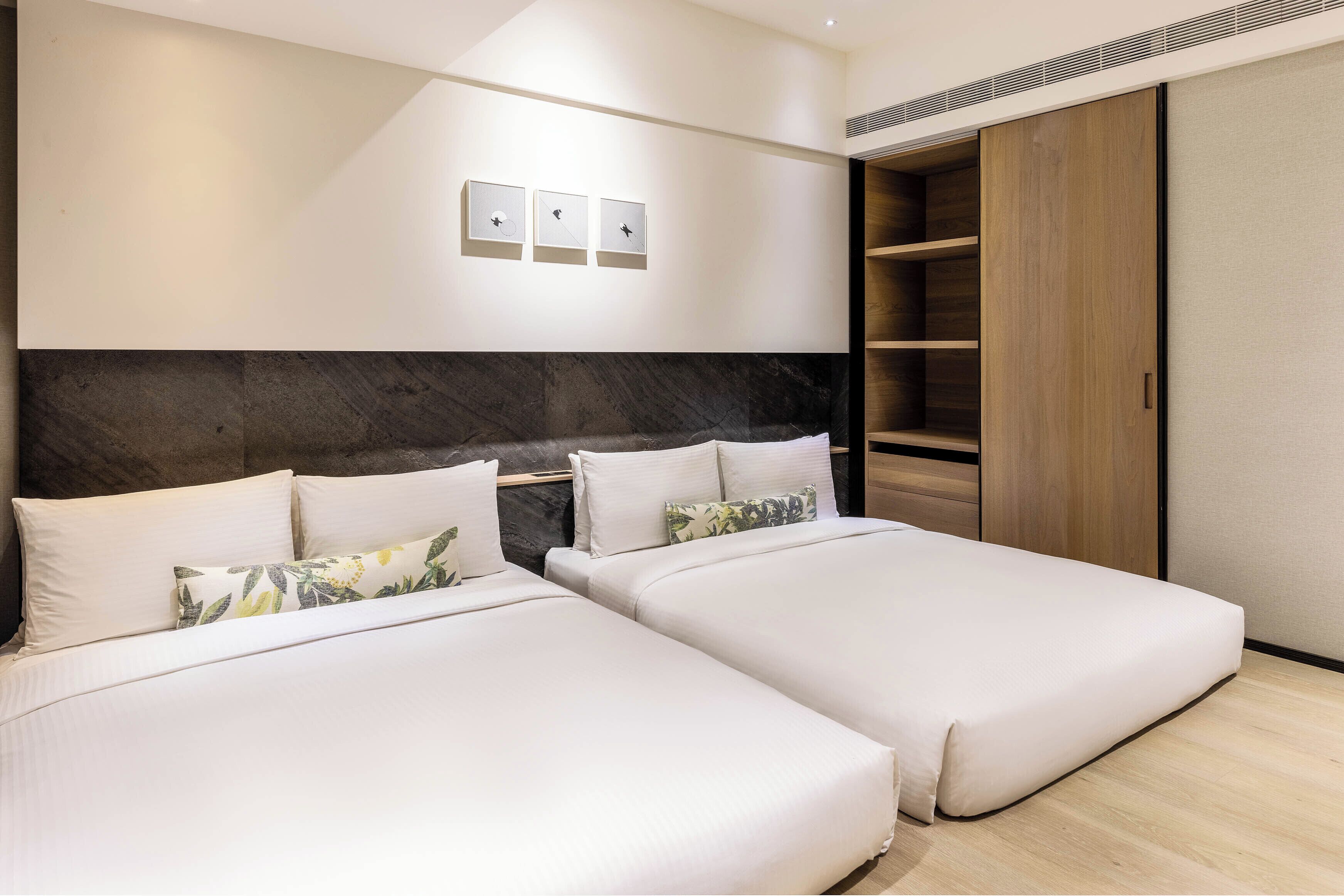 Ein modernes Hotelzimmer mit zwei Betten, einem großen Kleiderschrank und einer Wandleuchte.