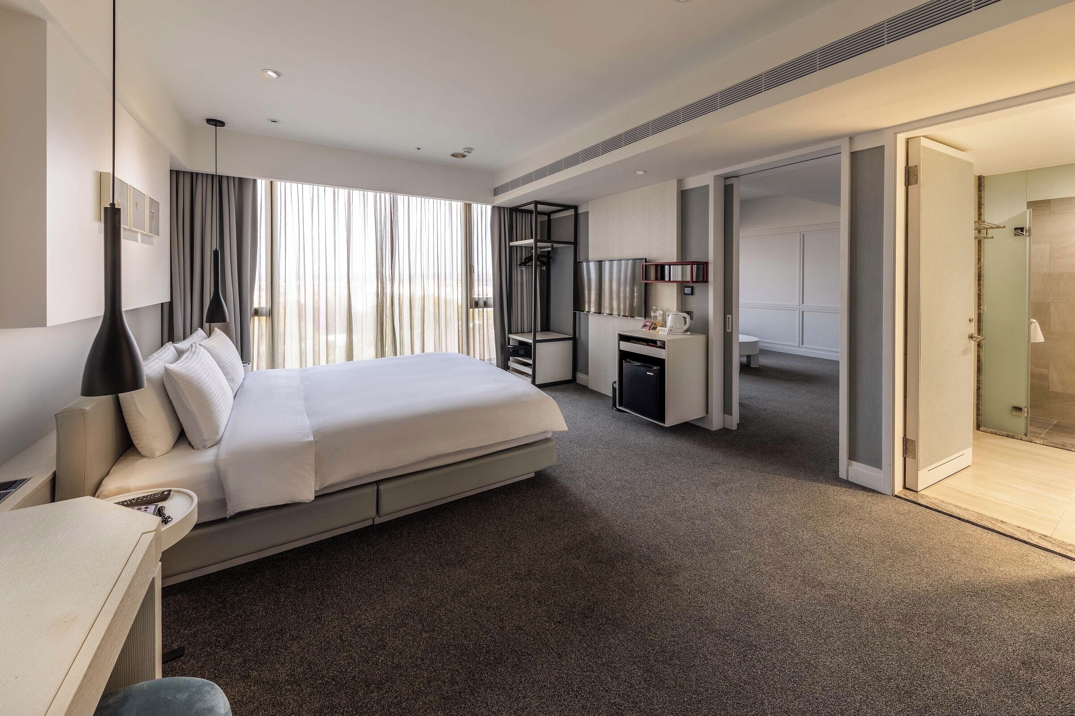 Une chambre d’hôtel moderne dotée d’un grand lit, d’un bureau, d’une petite kitchenette et d’un dressing.