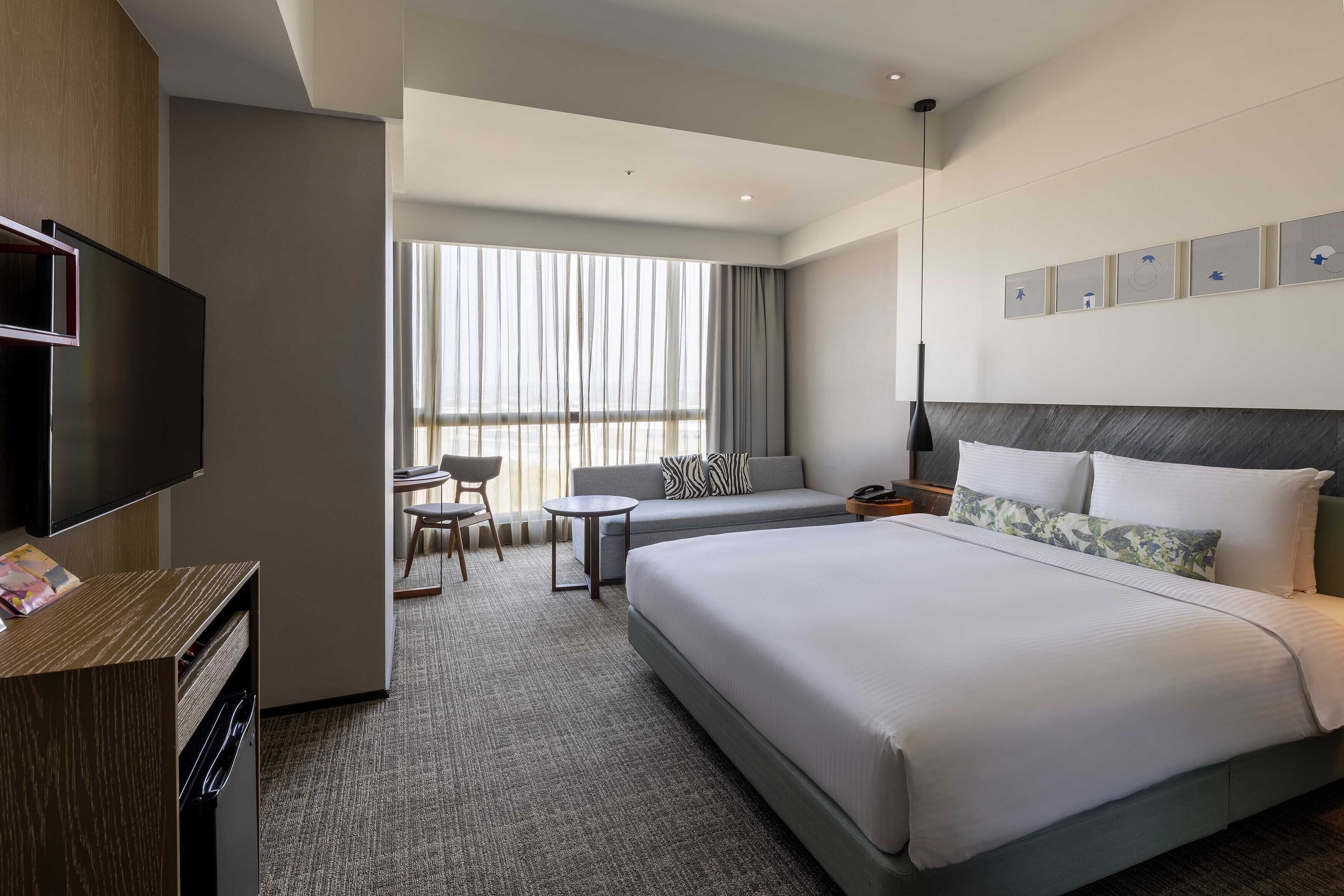 A hotel room with a large bed, a TV, a desk, and a seating area with a sofa and chairs.
