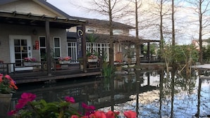 Un hotel a orillas del río con una terraza de madera, plantas en macetas y su reflejo en el agua.
