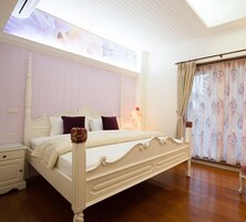 Un dormitorio con una cama grande, una mesita de noche, una ventana con cortinas florales y un tragaluz.