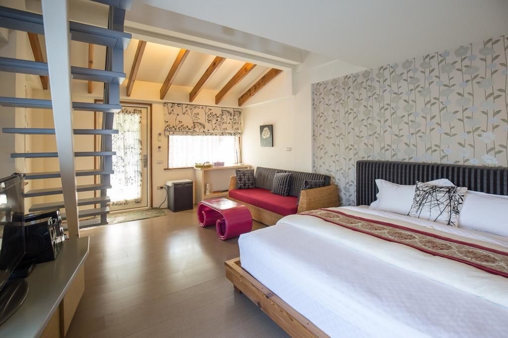 A bedroom with a large bed, a sofa, a small table, and a staircase.
