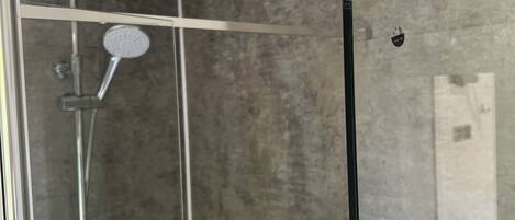 A modern shower enclosure with a glass door, a handheld showerhead, and a wall-mounted faucet.