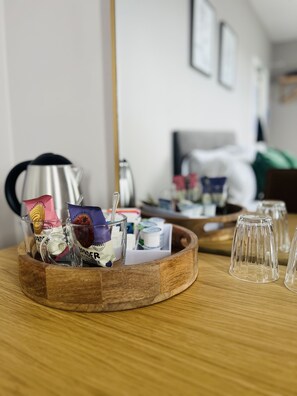 A wooden tray with various packaged snacks and a glass of water on a wooden table.