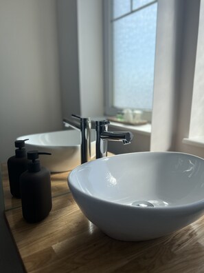 A bathroom with a white sink, a mirror, and two black soap dispensers on a wooden countertop.