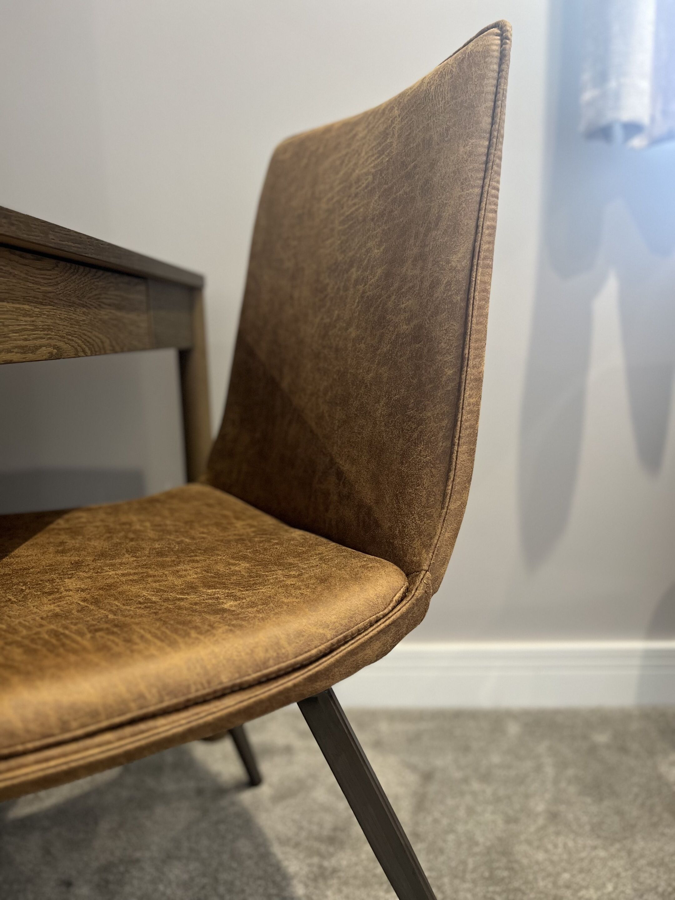 A close-up of a brown upholstered chair with a wooden table leg and a dark metal frame.