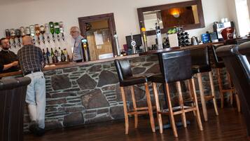 A bar area with a stone counter, multiple liquor bottles, and wooden bar stools.