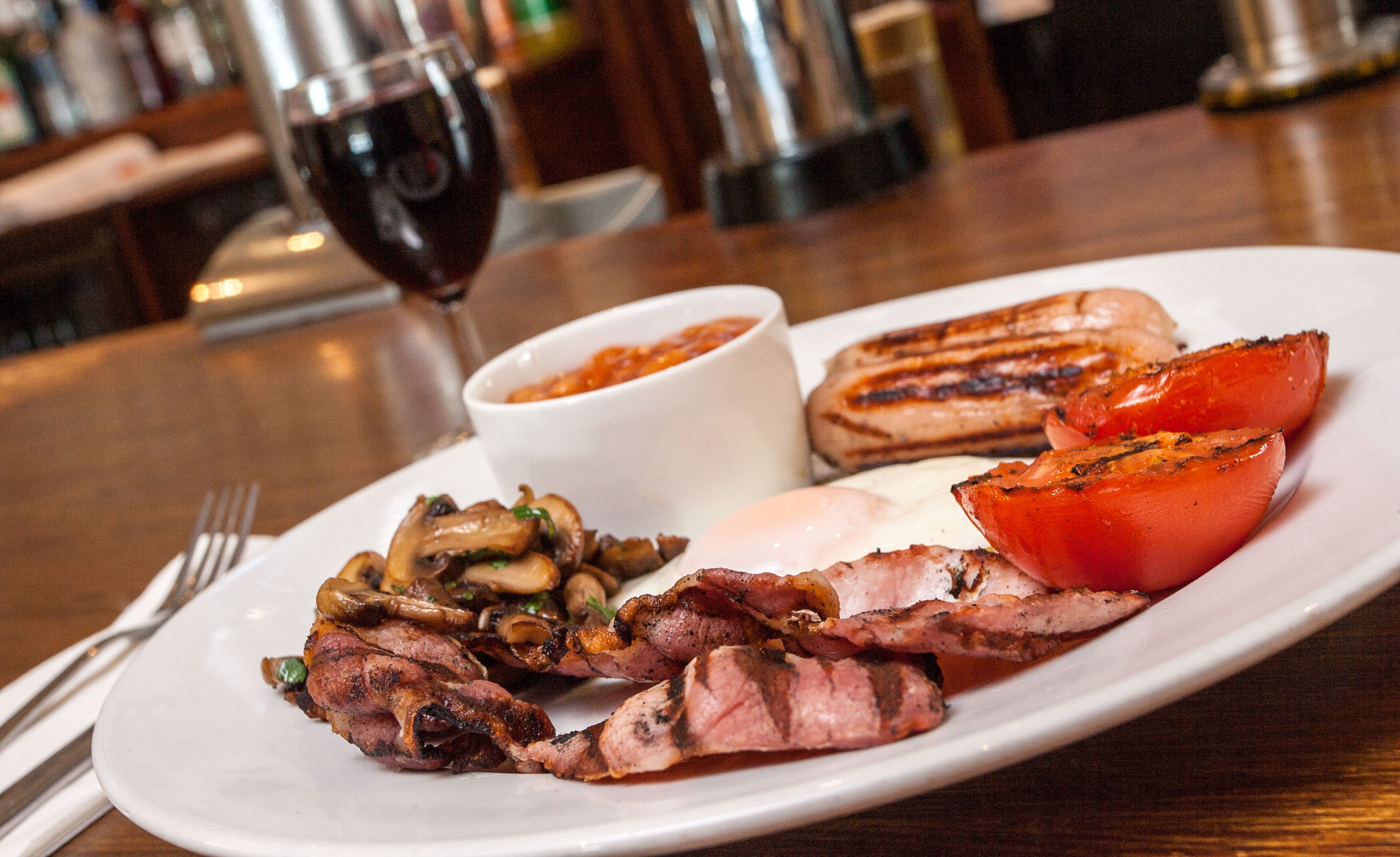 A plate of food including grilled meat, mushrooms, and tomatoes, with a glass of red wine in the background.