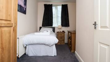 A bedroom with a bed, a nightstand, a dresser, a radiator, and a window with curtains.