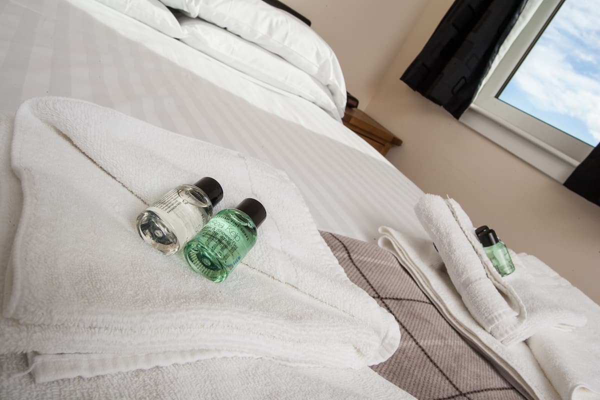 A neatly made bed with white linens and two bottles of lotion on a folded towel.
