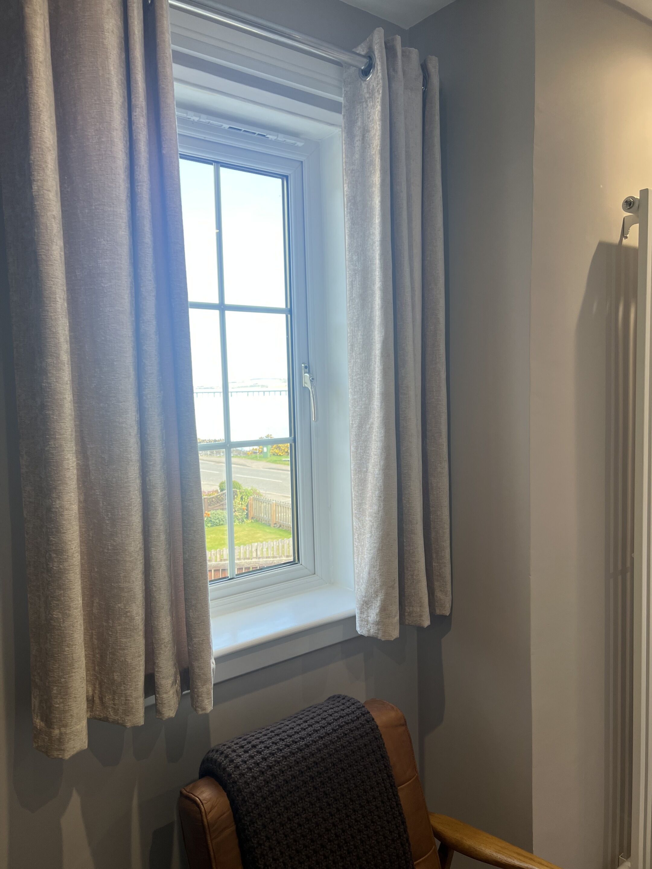 A room with a window, curtains, a chair, and a radiator.
