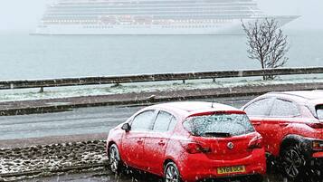 A red car parked on a wet surface with a cruise ship in the background.