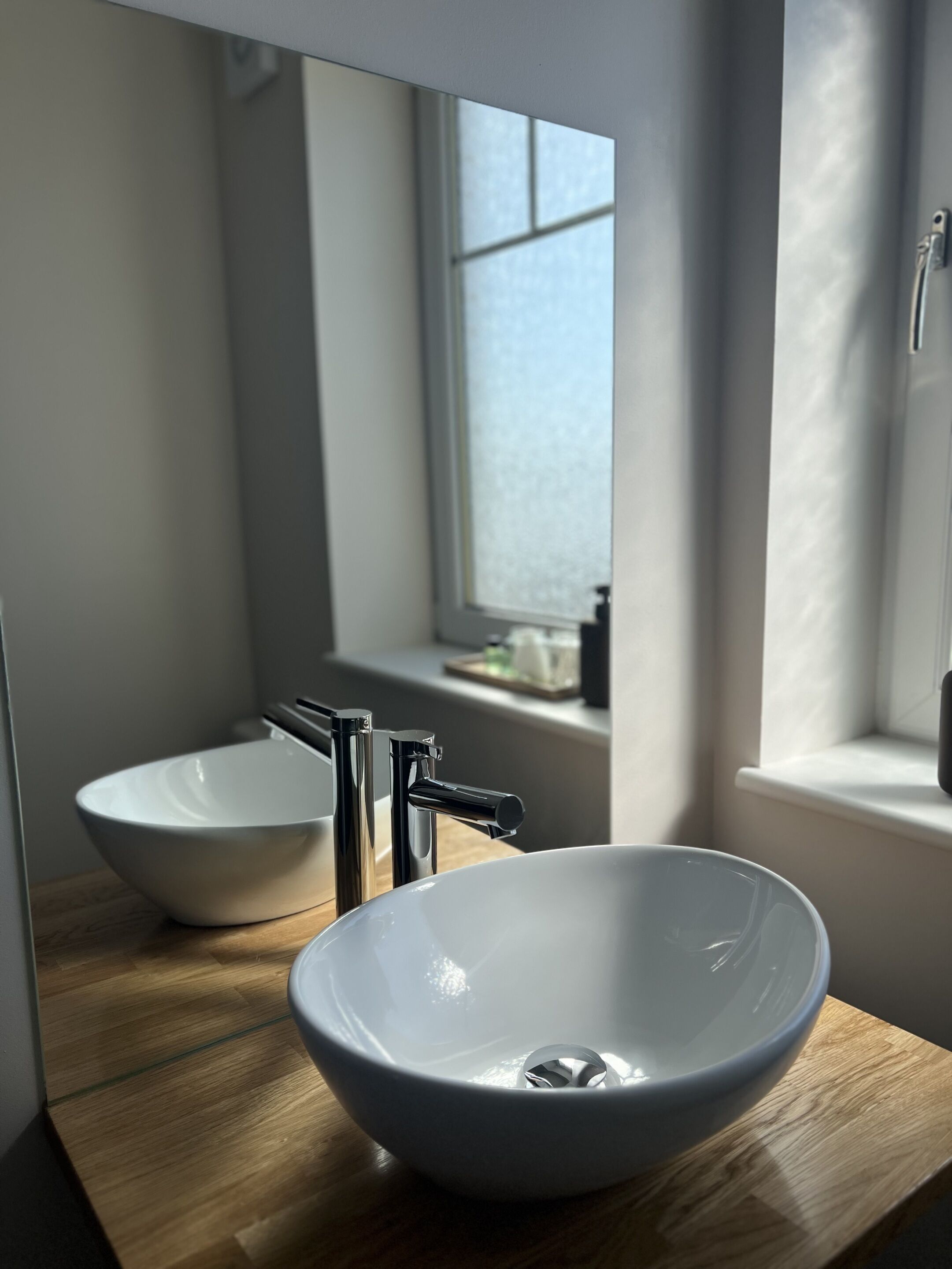 Un baño con lavamanos blanco, un espejo y una ventana.