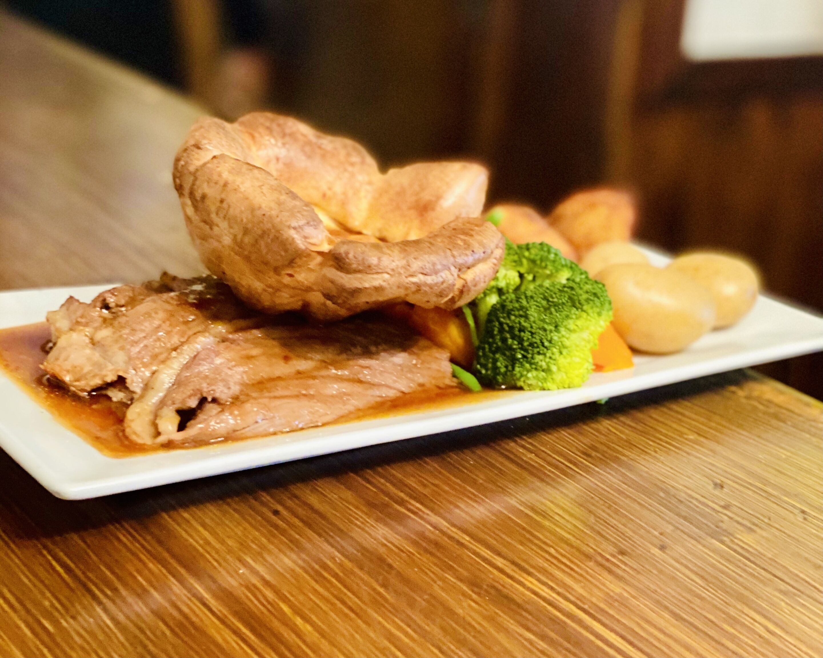 A plate of food with meat, broccoli, and potatoes on a wooden table.