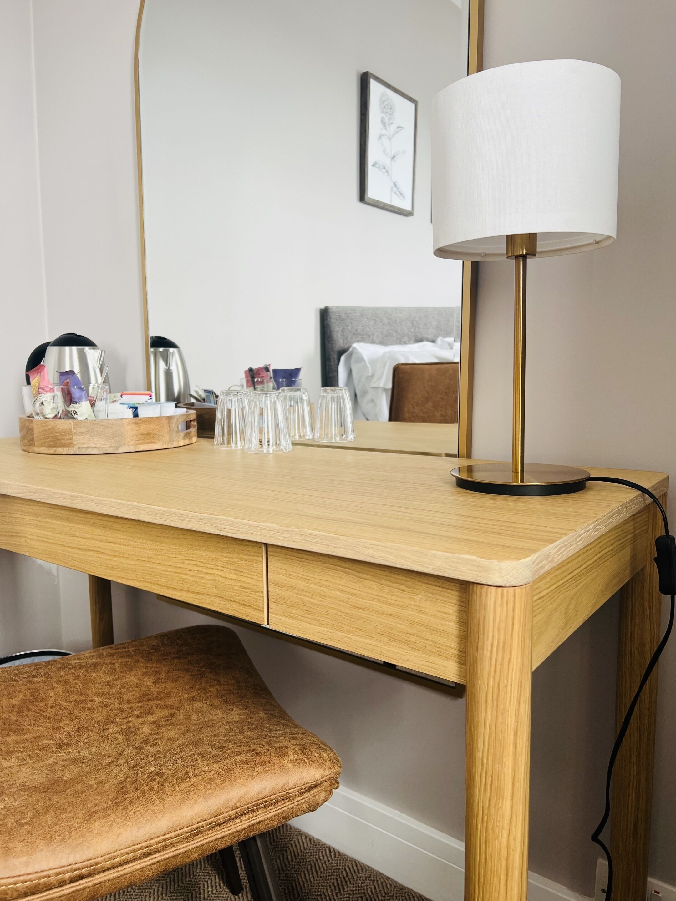 A hotel room with a wooden desk, a lamp, a chair, and a bed with a headboard.