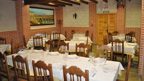 Un restaurant aux murs de briques, aux poutres apparentes et aux tables dressées pour le dîner.