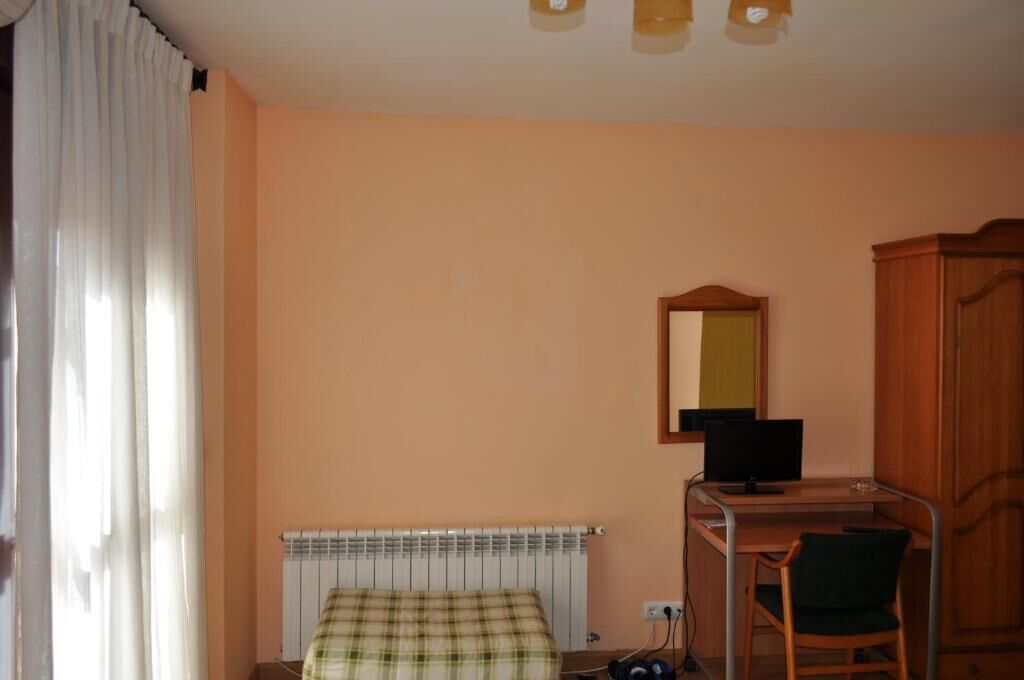 A bedroom with a bed, a desk with a computer, a chair, a wardrobe, and a radiator.