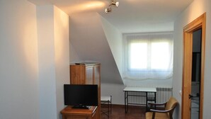 Une petite pièce bien éclairée, avec un téléviseur posé sur un meuble en bois, une table à manger entourée de chaises et une fenêtre avec des rideaux.
