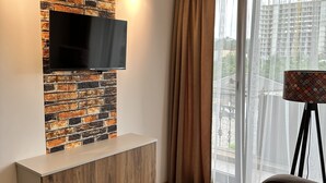 Un salon moderne avec un mur décoré d’un motif en briques, un téléviseur fixé au mur, un meuble en bois et une grande fenêtre avec des rideaux.