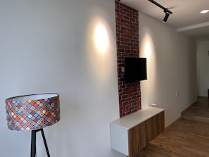 Un intérieur moderne avec un lampadaire à motifs, un téléviseur à écran plat fixé à un mur en briques et un banc en bois.