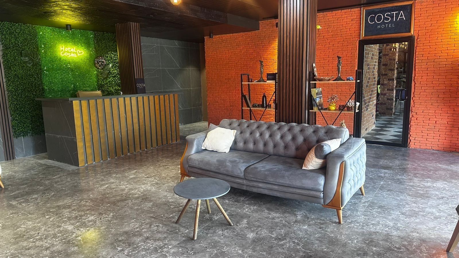 A reception area with a grey sofa, a small round table, and a green wall with a neon sign.