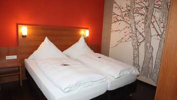 A double bed with white linens, a wooden headboard, and two bedside lamps.