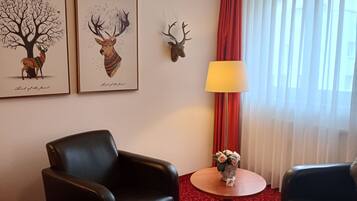 Habitación de hotel con dos sillones de cuero negro, una mesita redonda con un florero y una lámpara, junto a dos cuadros enmarcados que representan ciervos.
