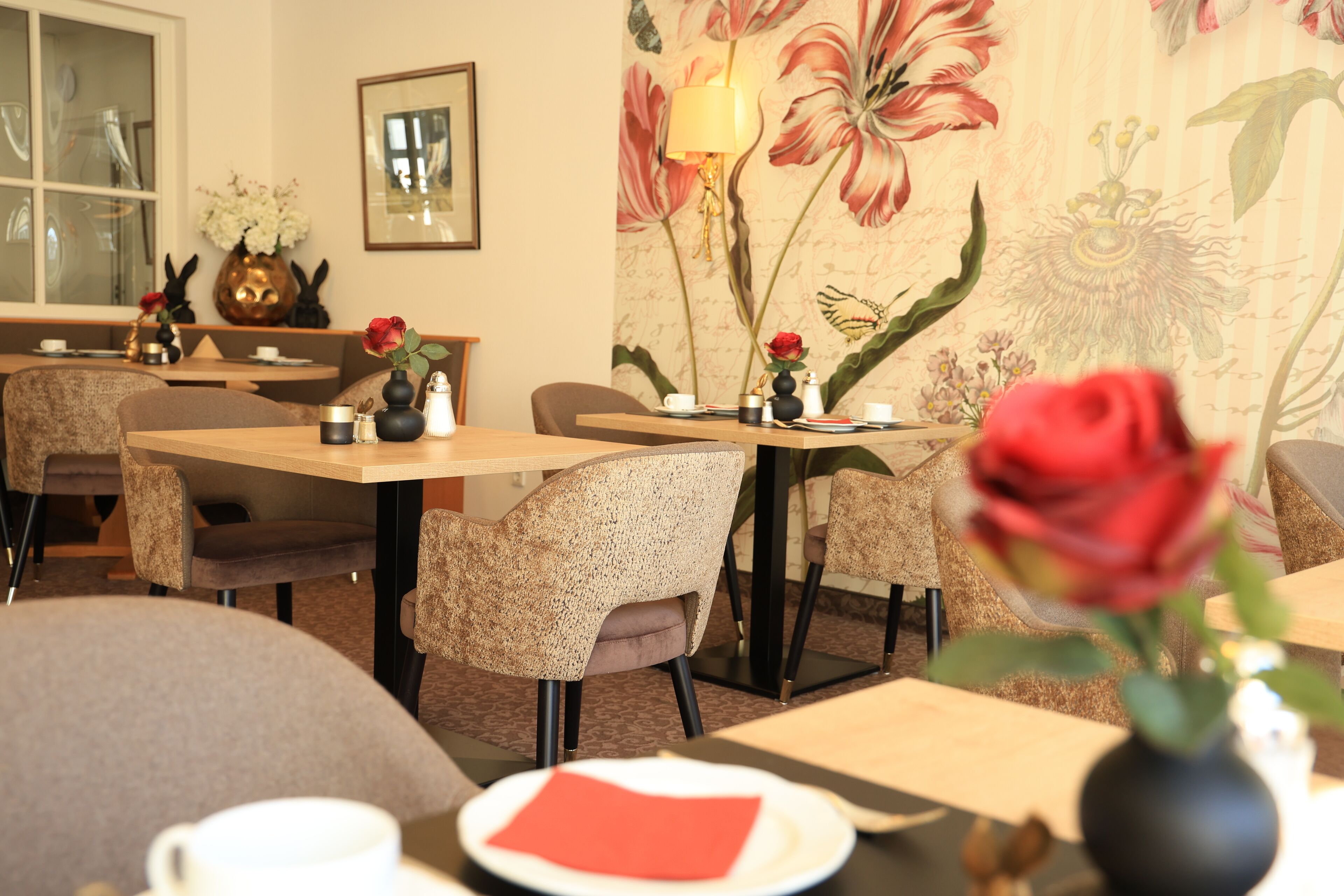 A dining area with tables, chairs, and floral wall art.