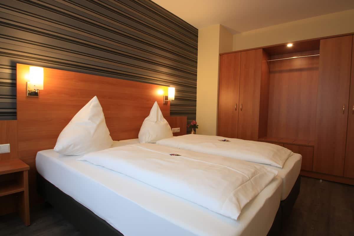Ein Doppelbett mit weißen Bettwäsche, ein hölzernes Kopfstück, zwei Wandlampen und ein Holzschrank.