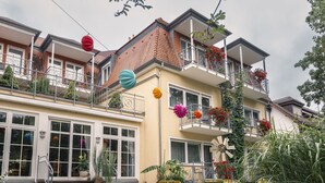 A two-story building with a balcony, outdoor seating area, and a garden with rocks and plants. - Hotel Alexa (Bad Mergentheim)