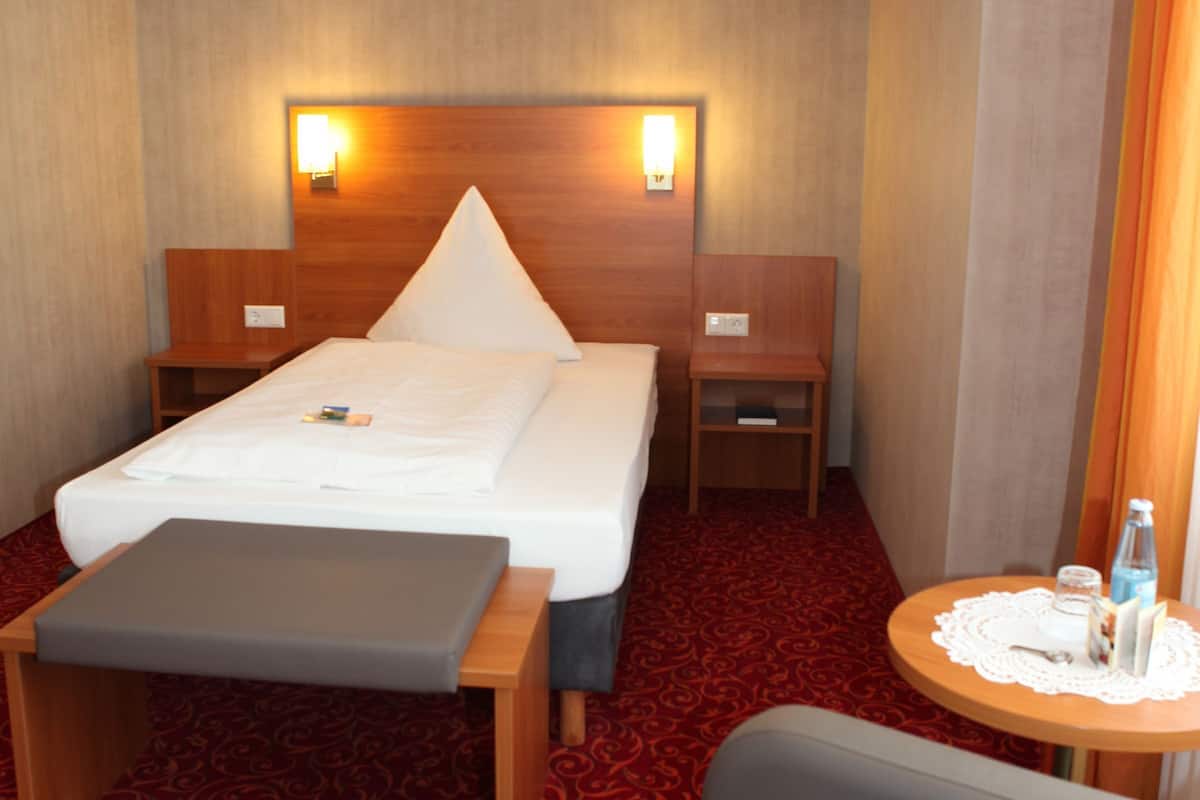 Ein Hotelzimmer mit einem Bett, Nachttischen, einem kleinen Tisch mit einer Flasche und einem Sessel.