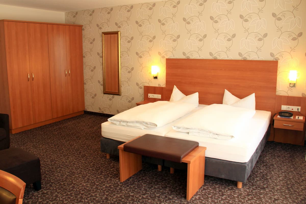 Ein Hotelzimmer mit Doppelbett, Holzschrank, Sitzbank und Nachttisch mit Lampe.