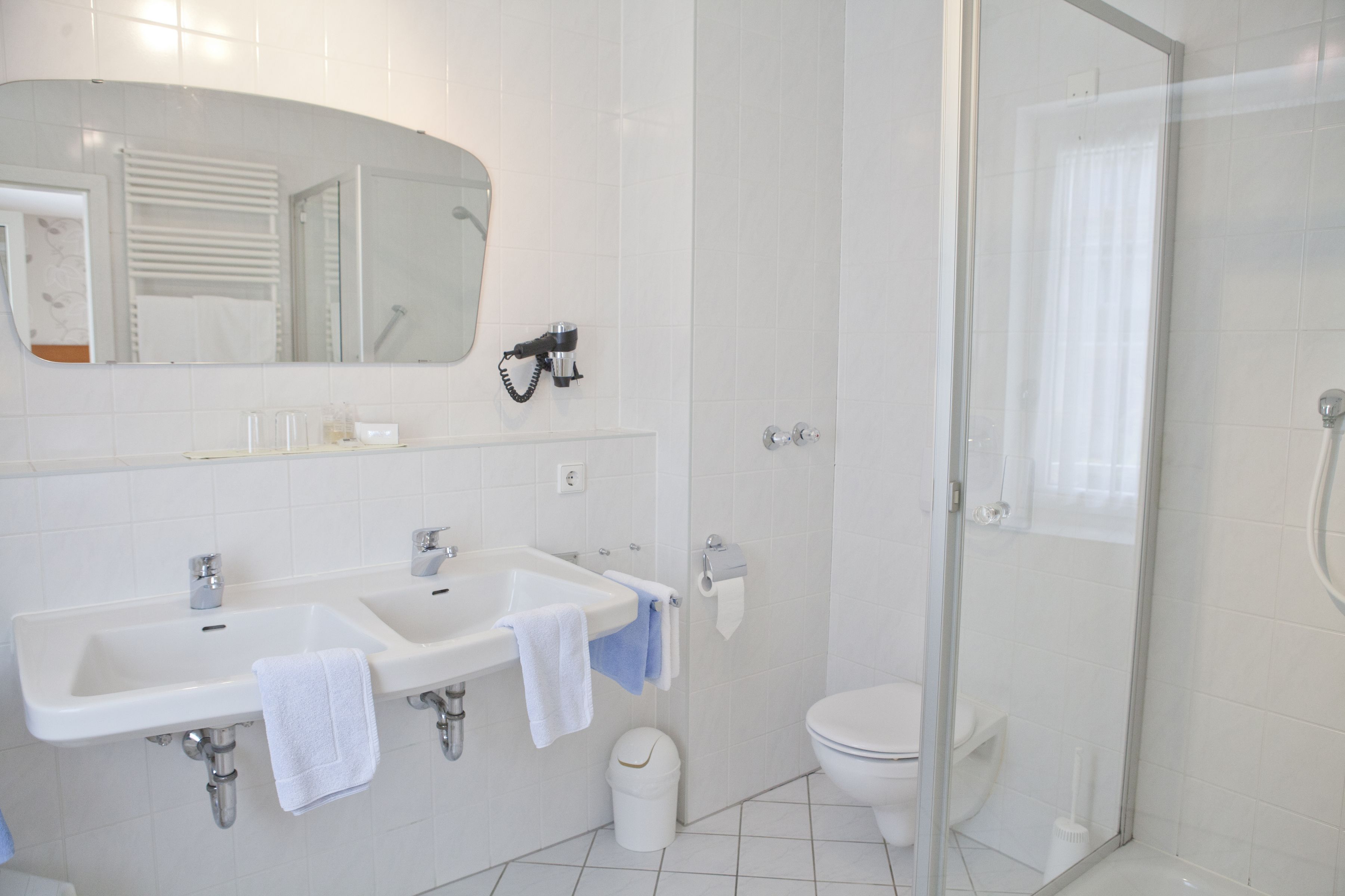 Un baño moderno con dos lavamanos, inodoro y ducha con mampara de vidrio.