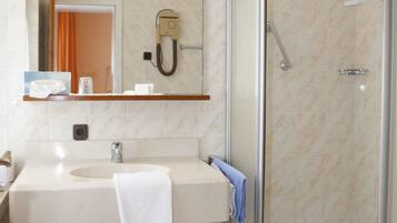 A bathroom with a marble-tiled floor, a sink with a towel, a mirror, and a glass-enclosed shower.