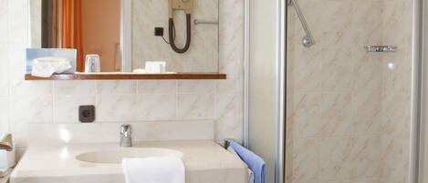 A bathroom with a marble-tiled floor, a sink with a towel, a mirror, and a glass-enclosed shower.