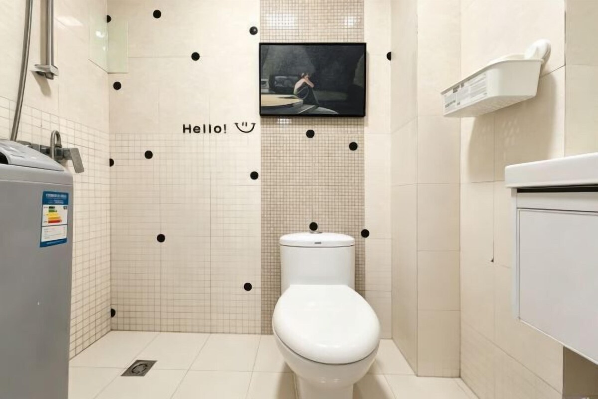 A bathroom with a toilet, a sink, a mirror, and a television mounted on the wall.