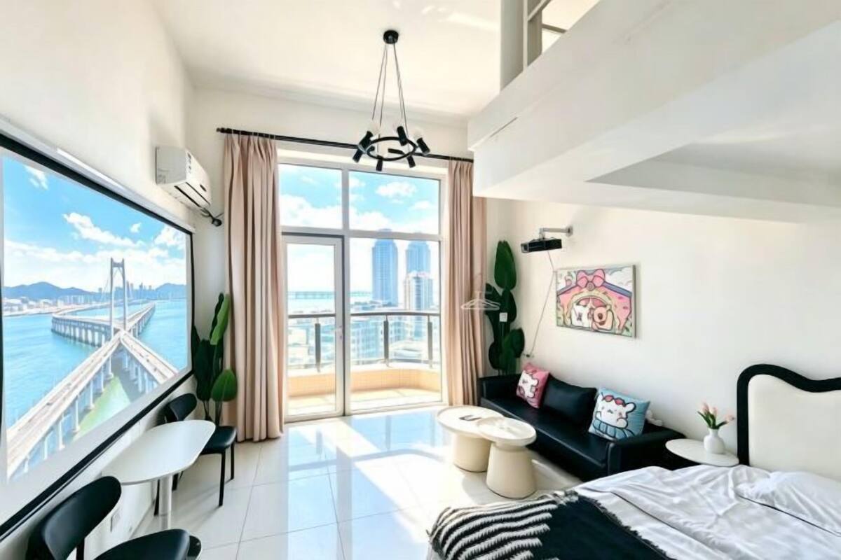 Une chambre d’hôtel moderne avec une grande fenêtre, un lit, un canapé, une petite table et une chaise.