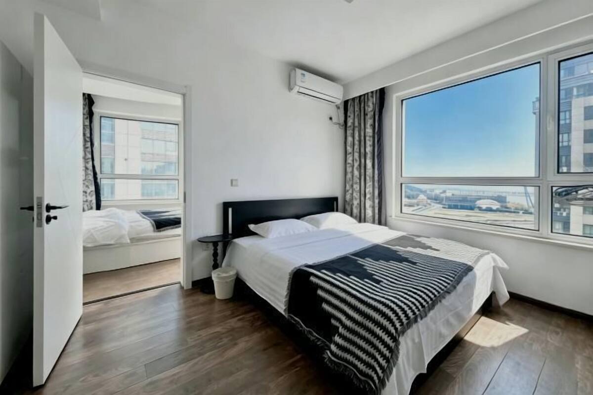 Une chambre avec un lit, une fenêtre, un appareil de climatisation et une vue sur les immeubles.